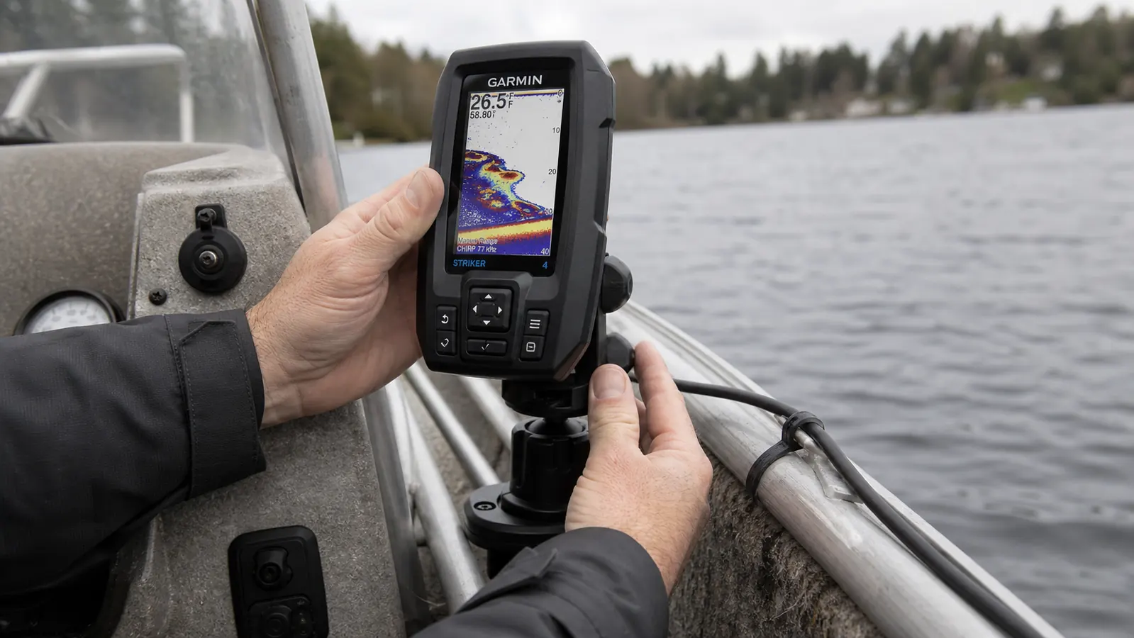 Close-up of a hand mounting a Garmin Striker 4 fish finder display to the console of a small aluminum boat