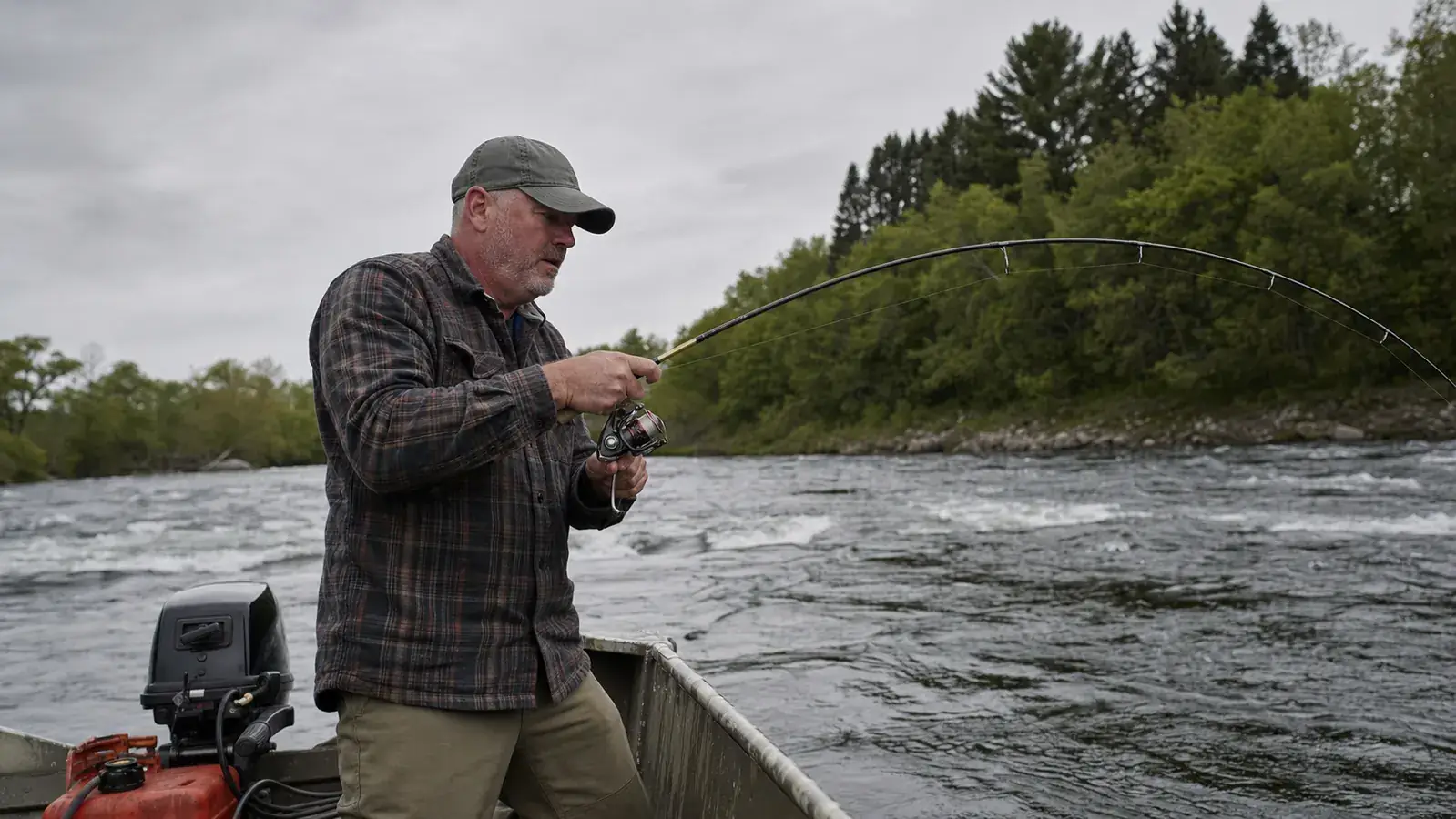 Angler fighting a smallmouth bass on light spinning tackle from an aluminum boat on a river