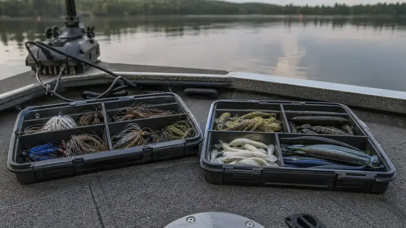 Two open tackle trays side by side on a boat deck, one KastKing and one Plano StowAway, loaded with lures